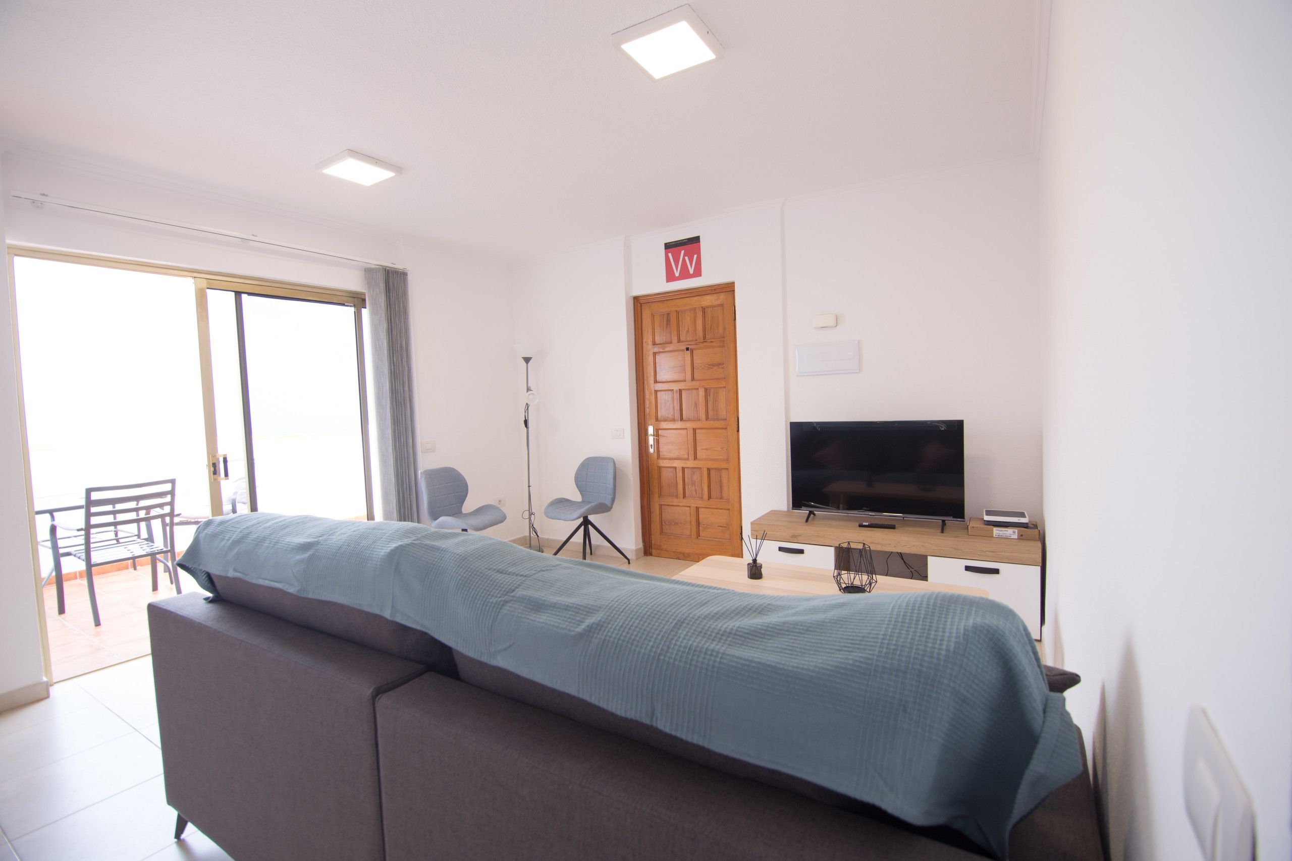 A hotel room with a bed, a desk with a TV, a chair, and a door.