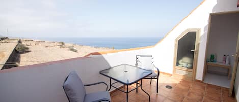 A balcony with a table and chairs, overlooking a beach and ocean.