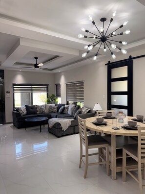 Uma sala de estar moderna com um sofá seccional, uma mesa de jantar posta para quatro pessoas e um ventilador de teto.