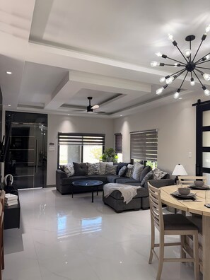 Un salon moderne avec un canapé d’angle, une table à manger et un ventilateur de plafond.
