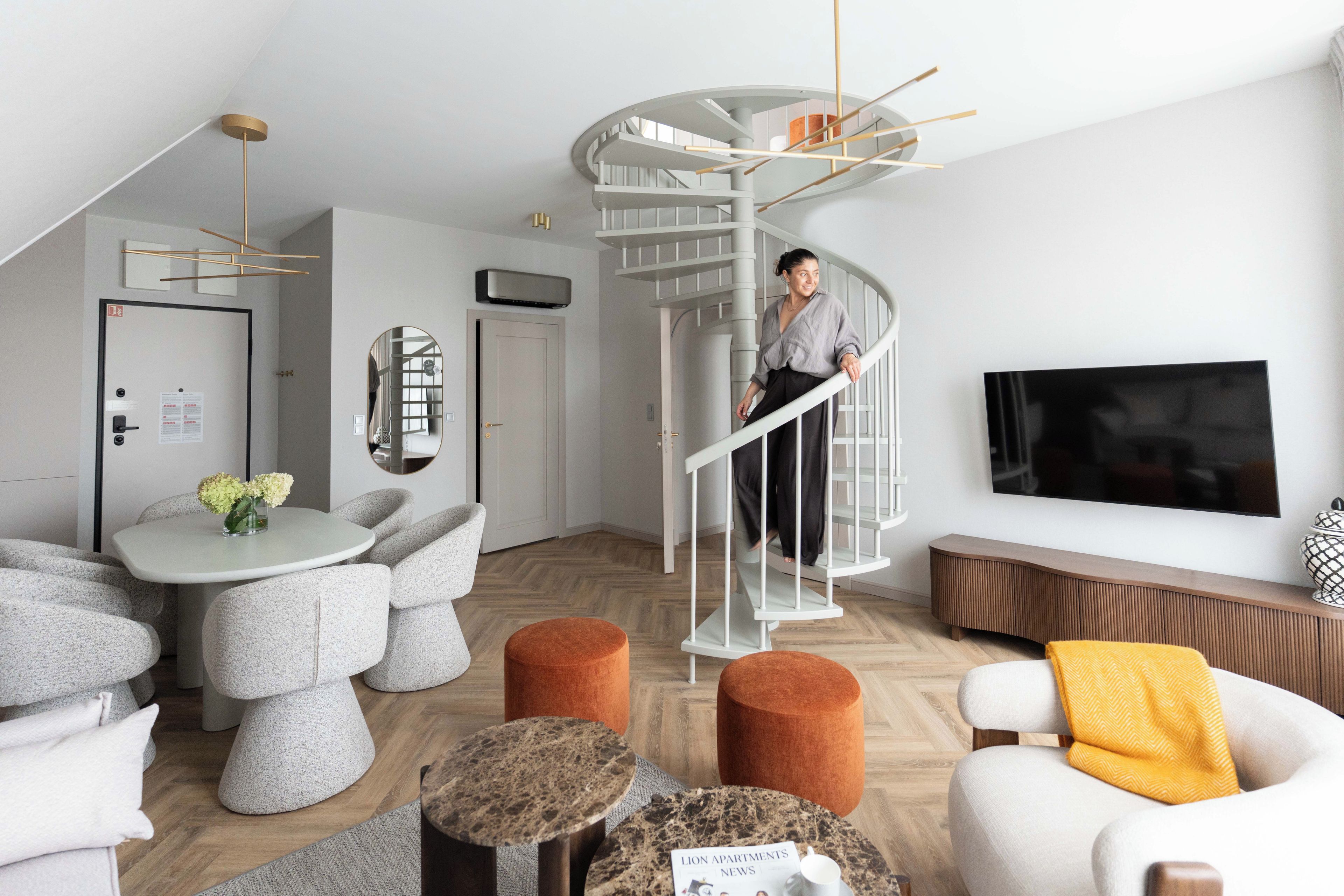 A modern living room with a spiral staircase, a dining area with a round table, and a television mounted on the wall.