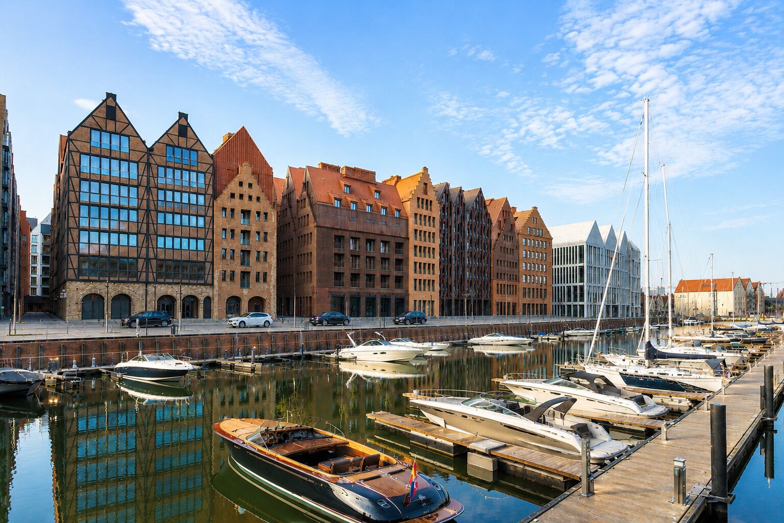 En lystbådehavn med fortøjede både, en bygning ved vandet med moderne arkitektur, og en klar himmel.