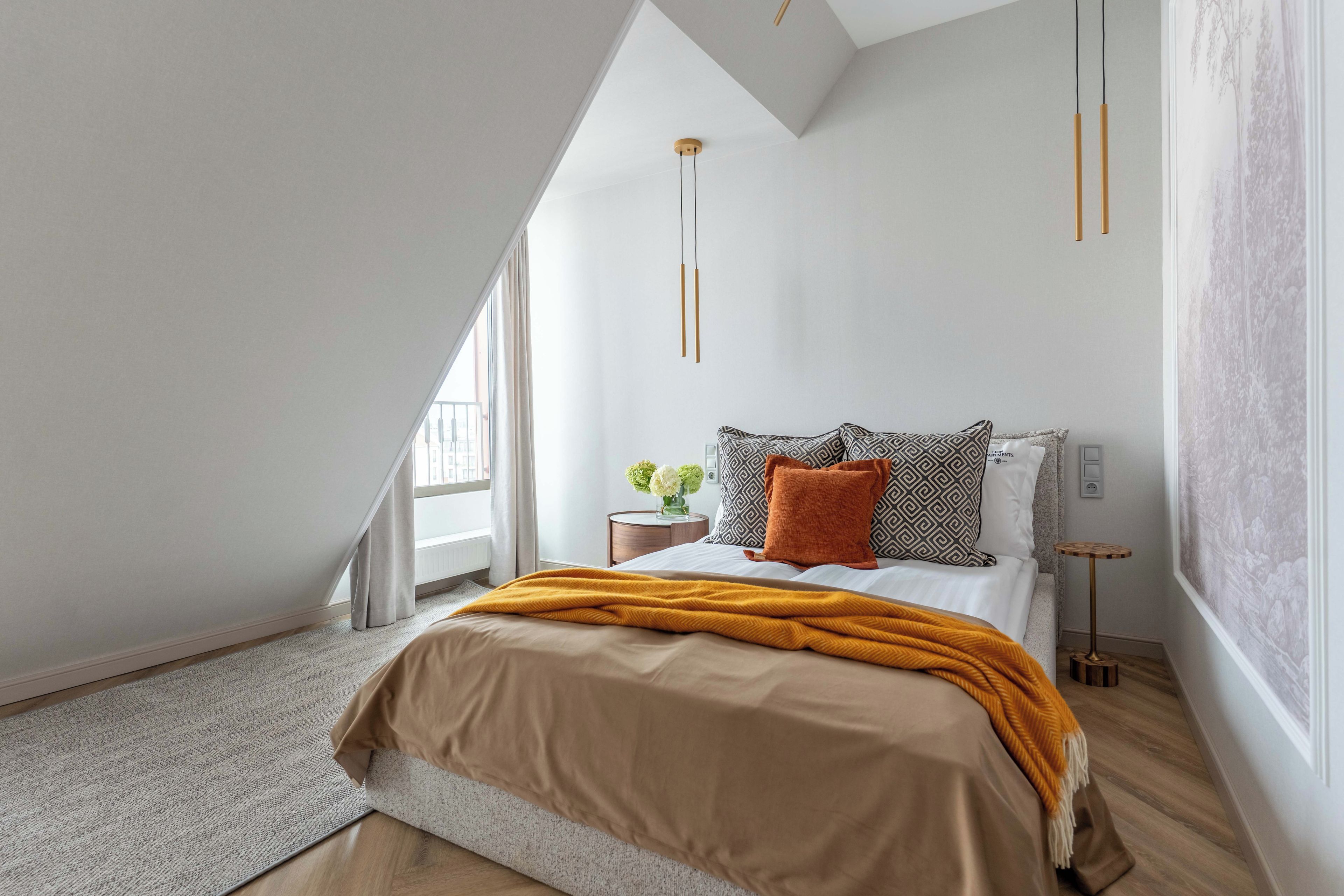 A bedroom with a sloped ceiling, a bed with a patterned pillow, a small bedside table with a vase, and a hanging light fixture.