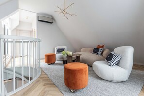 Uma sala de estar moderna com um berço branco, um sofá cinzento e pufes laranja.