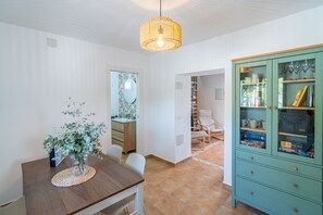 A dining area with a wooden table, chairs, a hanging light fixture, and a cabinet with glass doors. - Cubo's Casa El Farol / Private pool / BBQ / Free Wi-Fi (Alhaurín el Grande)