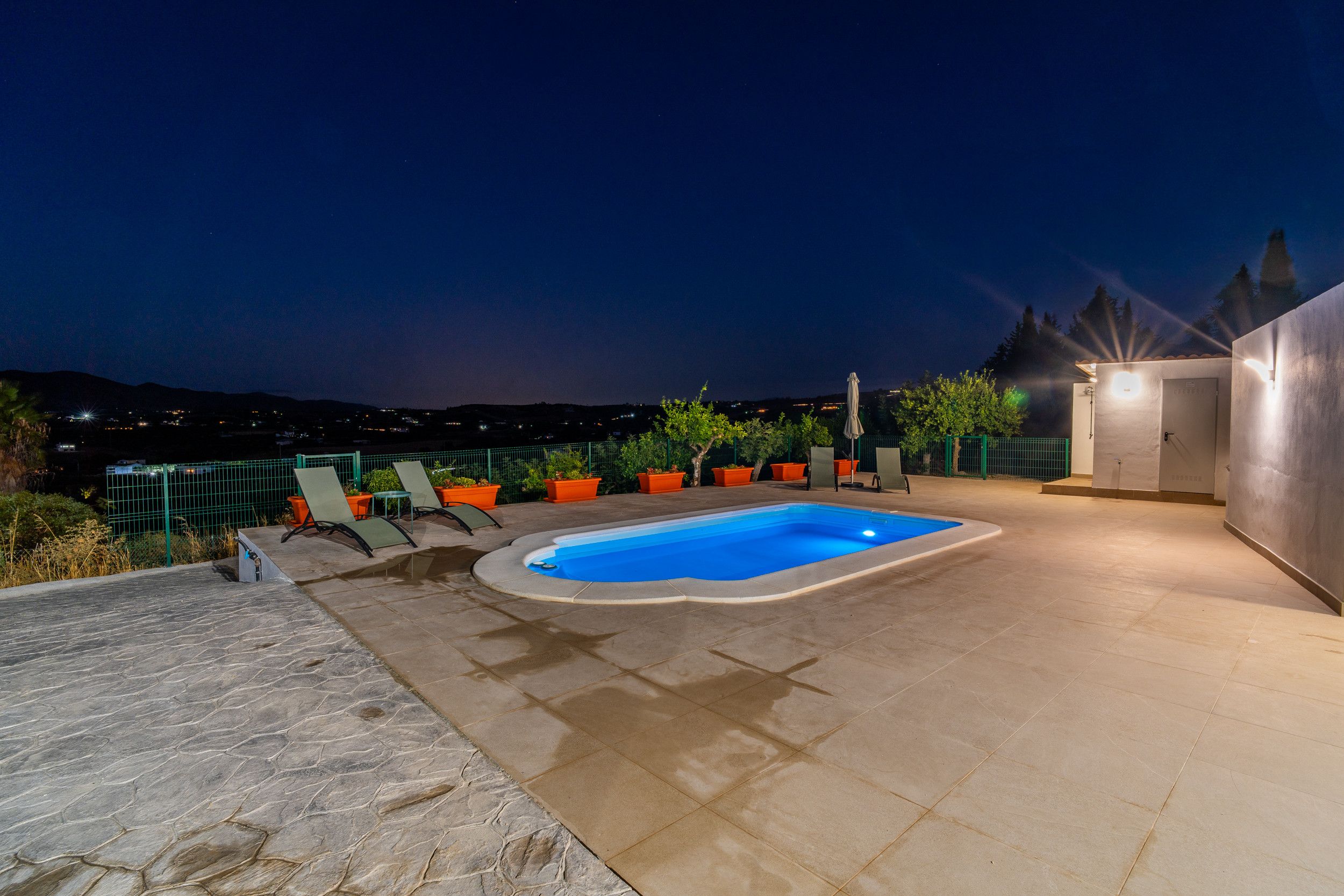 An outdoor swimming pool with lounge chairs and potted plants, surrounded by a stone patio.