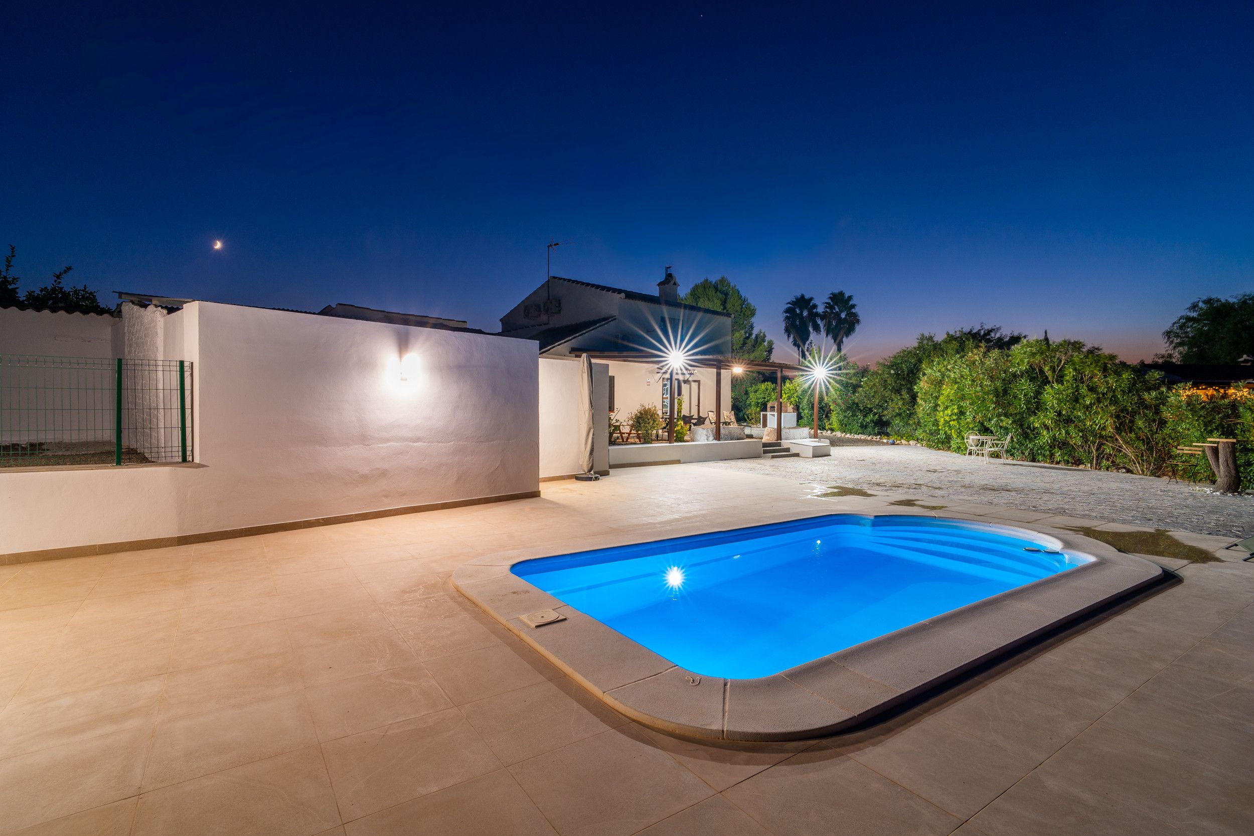 A swimming pool with a clear blue water surface, surrounded by a paved patio area.