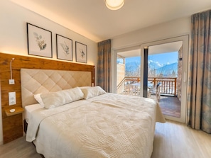 Une chambre dotée d’un grand lit, d’une tête de lit en bois et d’un balcon avec un espace salon extérieur.