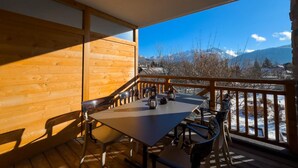 Un terrazza in legno con tavolo e sedie, affacciata su un paesaggio montano innevato.
