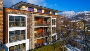 Un edificio a più piani con ampie finestre, balconi e vista sulle montagne innevate.