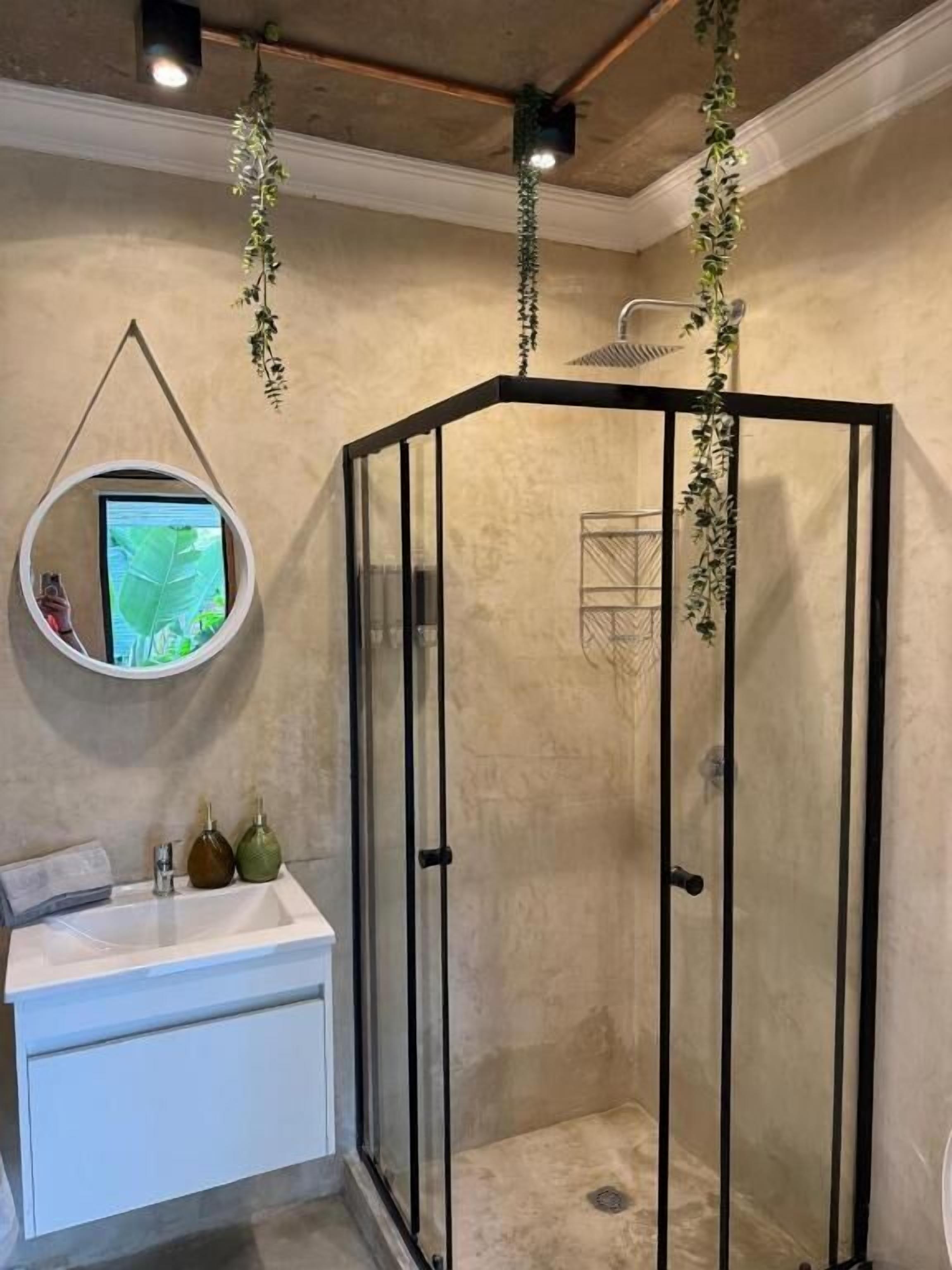 A bathroom with a glass-enclosed shower, a white sink, and a round mirror.