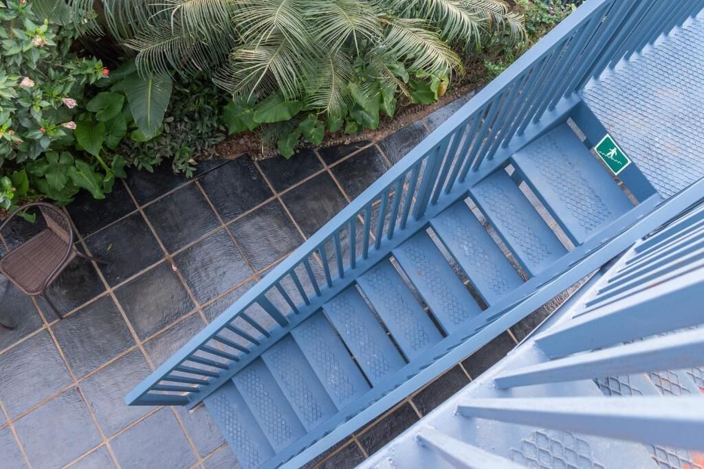 A blue metal staircase with a green emergency exit sign, surrounded by greenery and a tiled floor.