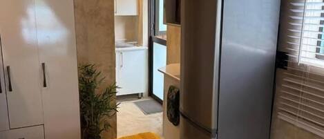 Una cocina compacta con refrigerador, armarios y una cama con colcha estampada.