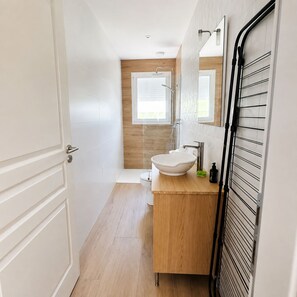 Ein modernes Badezimmer mit einem Holzbadezimmer-Möbelstück, einem weißen Waschbecken und einer Duschkabine aus Glas.