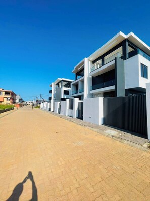 A modern residential street with contemporary houses, a paved walkway, and a clear blue sky.
