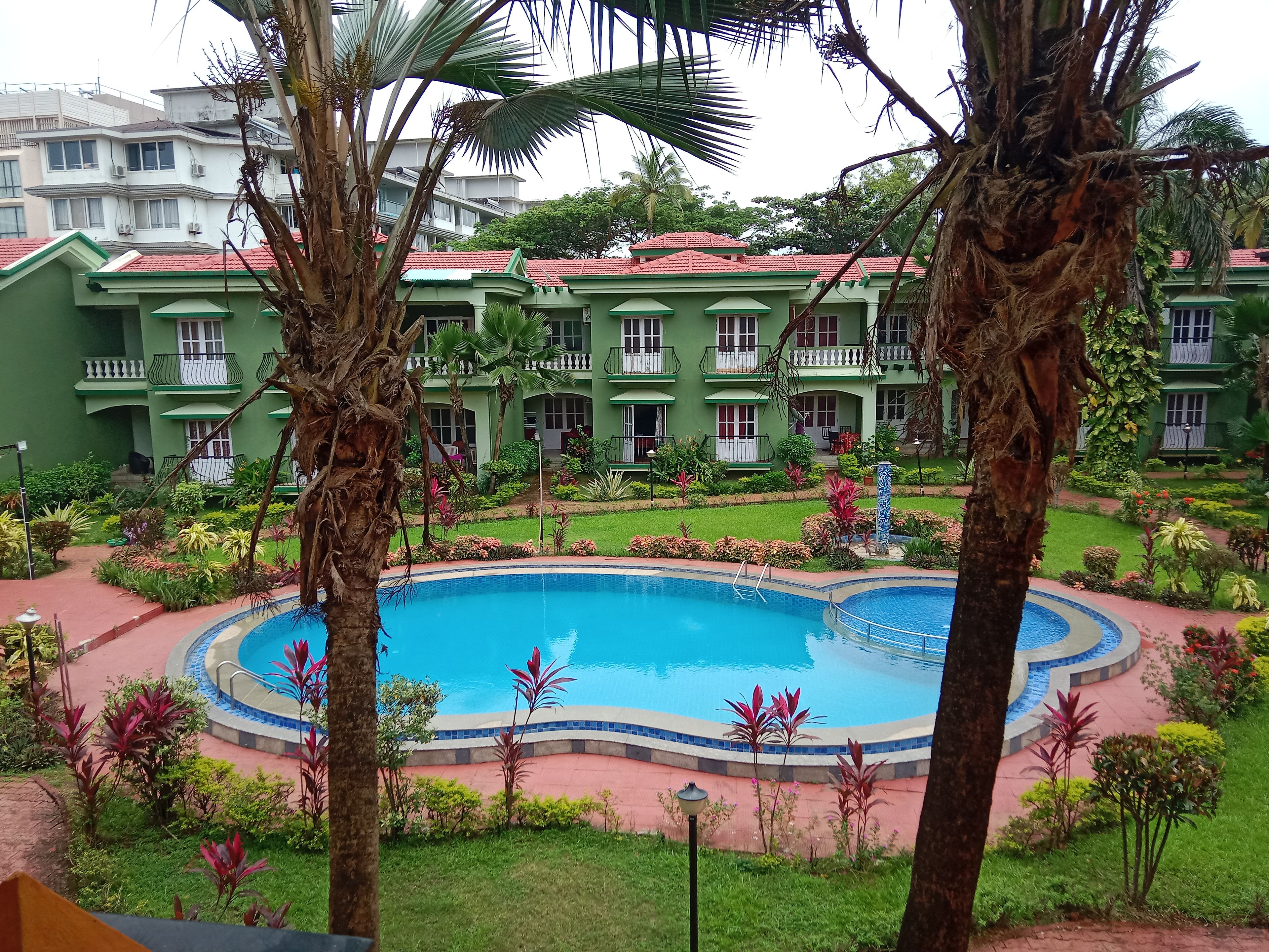 Un hotel con piscina rodeado de exuberante vegetación y un edificio de varios pisos con balcones.