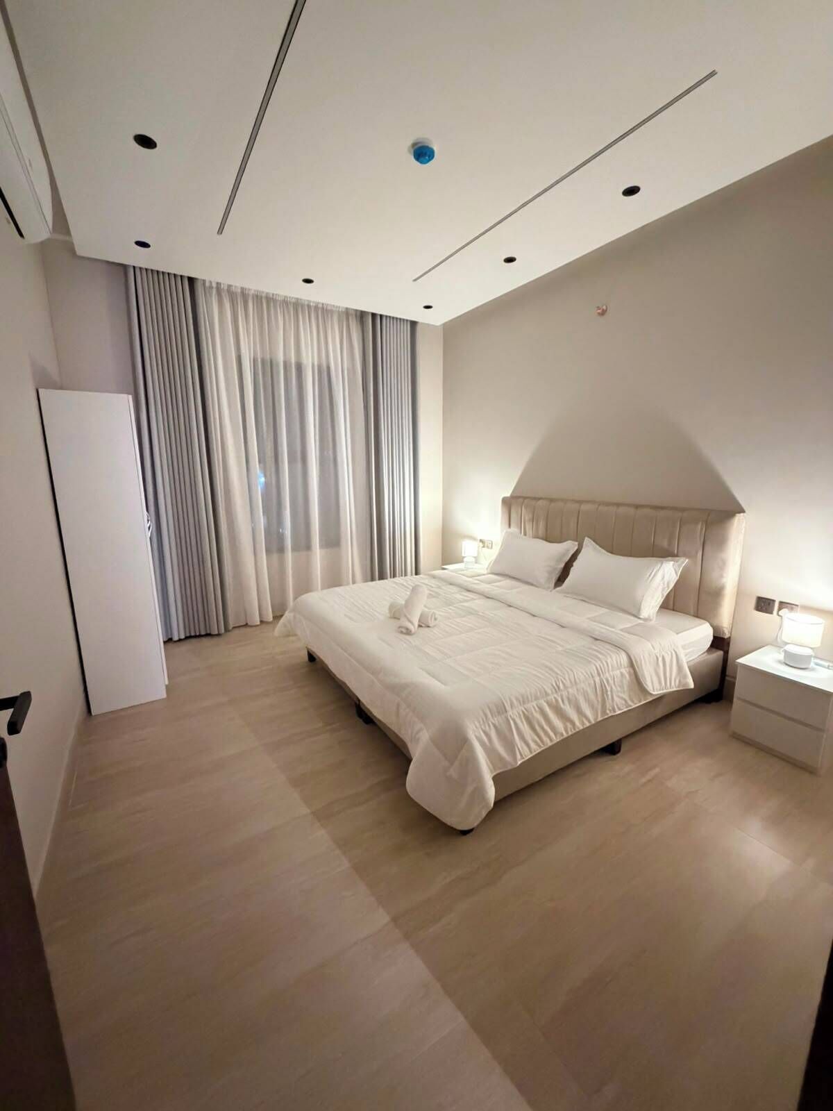A modern bedroom with a large bed, a bedside table, and a wardrobe.