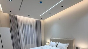 Et moderne soveværelse med en stor seng, et natbord, en lampe og et vindue med gardiner.