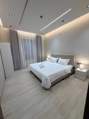 Ein modernes Schlafzimmer mit einem großen Bett, einem Nachttisch, einer Lampe und einem Fenster mit Vorhängen.