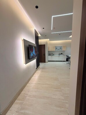 A modern kitchen with white cabinets, a flat-screen TV mounted on the wall, and a wooden door.