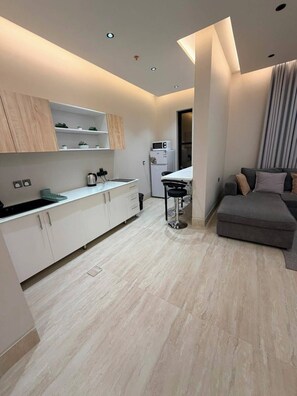 A modern kitchen with white cabinets, a black countertop, and a microwave. There is a dining area with a grey sofa and a small table.