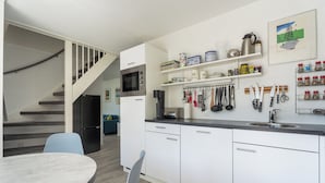 A modern kitchen with white cabinets, a built-in microwave, and a coffee machine. There is a dining area with a table and chairs, and a staircase leading to another level. - Vacation Home Wolphaarsdijk 9b (Wolphaartsdijk)