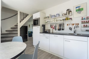 A modern kitchen with white cabinets, a built-in microwave, and a coffee machine. There is a dining area with a table and chairs, and a staircase leading to another level. - Vacation Home Wolphaarsdijk 9b (Wolphaartsdijk)