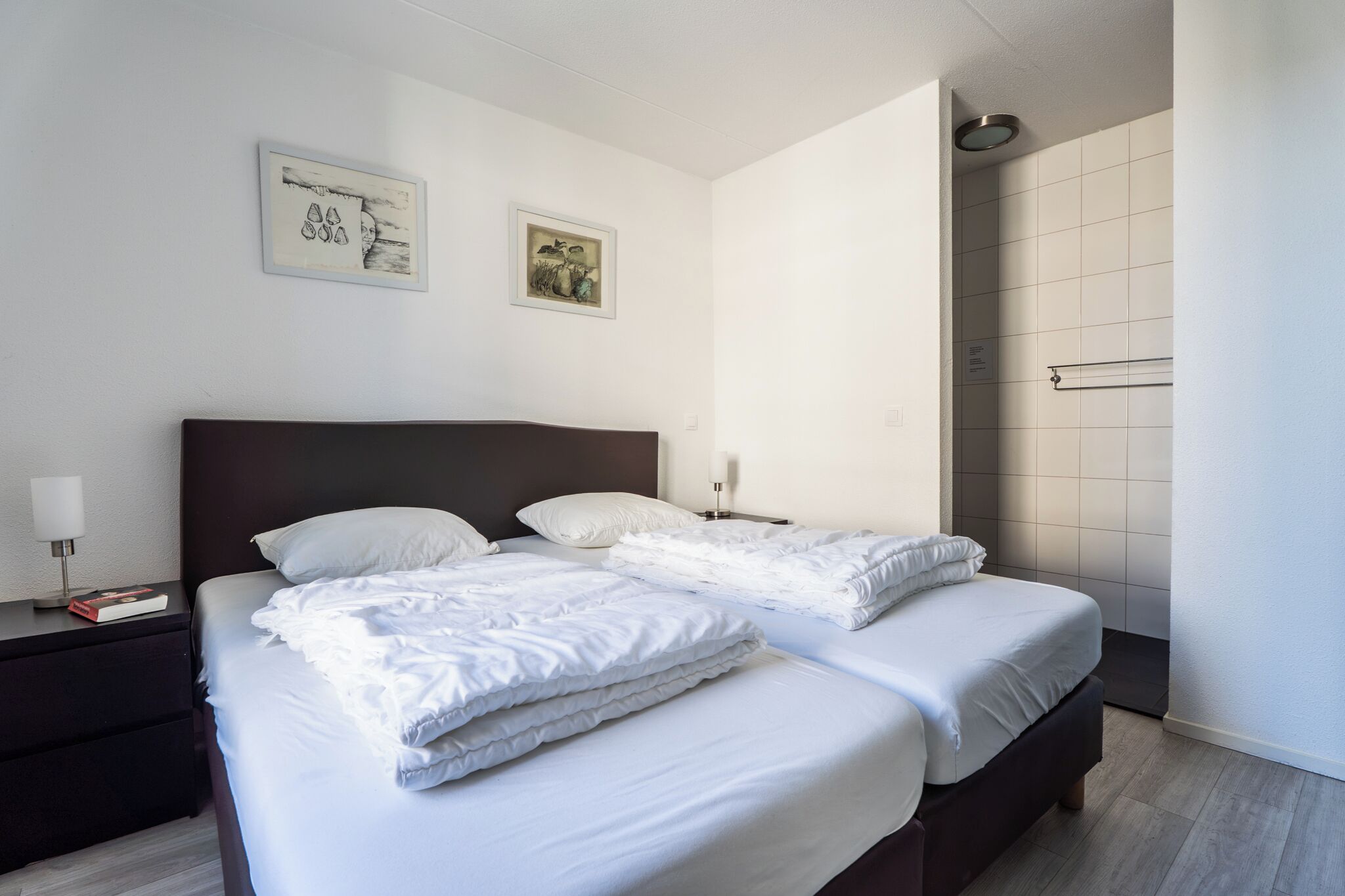 Ein Hotelzimmer mit zwei Betten, einem Nachttisch, einer Nachttischlampe und einem gerahmten Bild an der Wand.