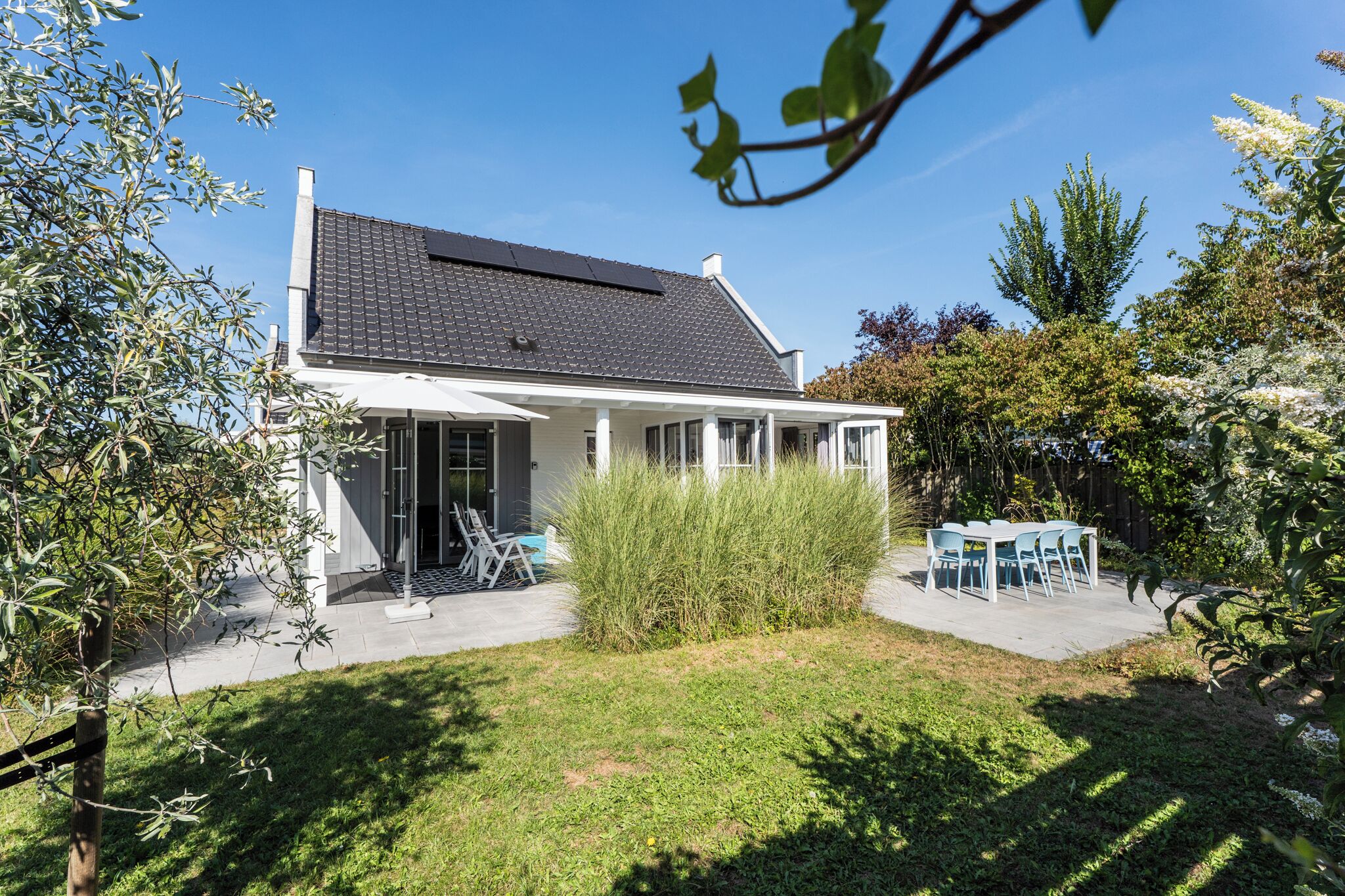 Ein Haus mit überdachter Terrasse, einem Schwimmbecken und einem Garten mit Tisch und Stühlen.