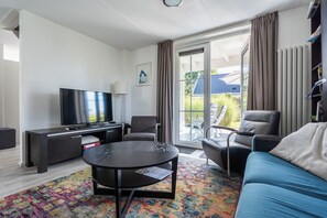 Una sala de estar moderna con una televisión de pantalla plana, un sofá, una mesa de centro y un balcón con vistas.