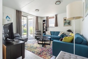 A modern living room with a sofa, armchair, coffee table, and a television. - Vacation Home Wolphaarsdijk 9b (Wolphaartsdijk)