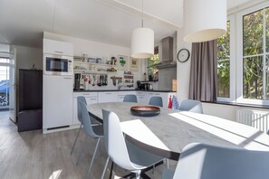 Una cocina moderna con armarios blancos, una mesa de comedor con sillas y un amplio ventanal con cortinas.
