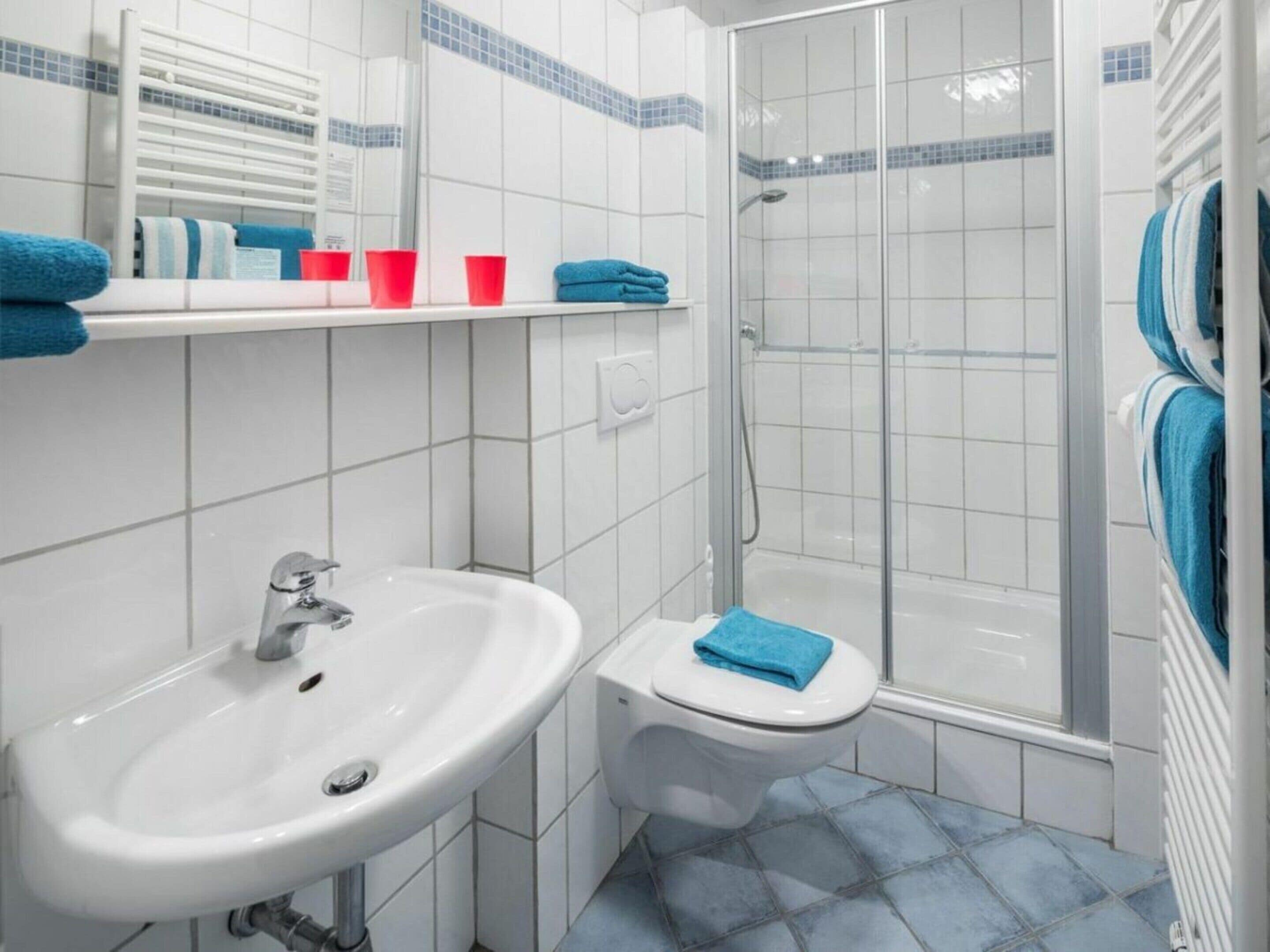 Une salle de bain avec un lavabo blanc, des toilettes, une douche en verre et un sol carrelé.