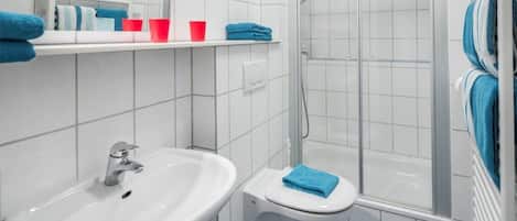 Une salle de bain avec un lavabo blanc, des toilettes, une douche en verre et un sol carrelé.