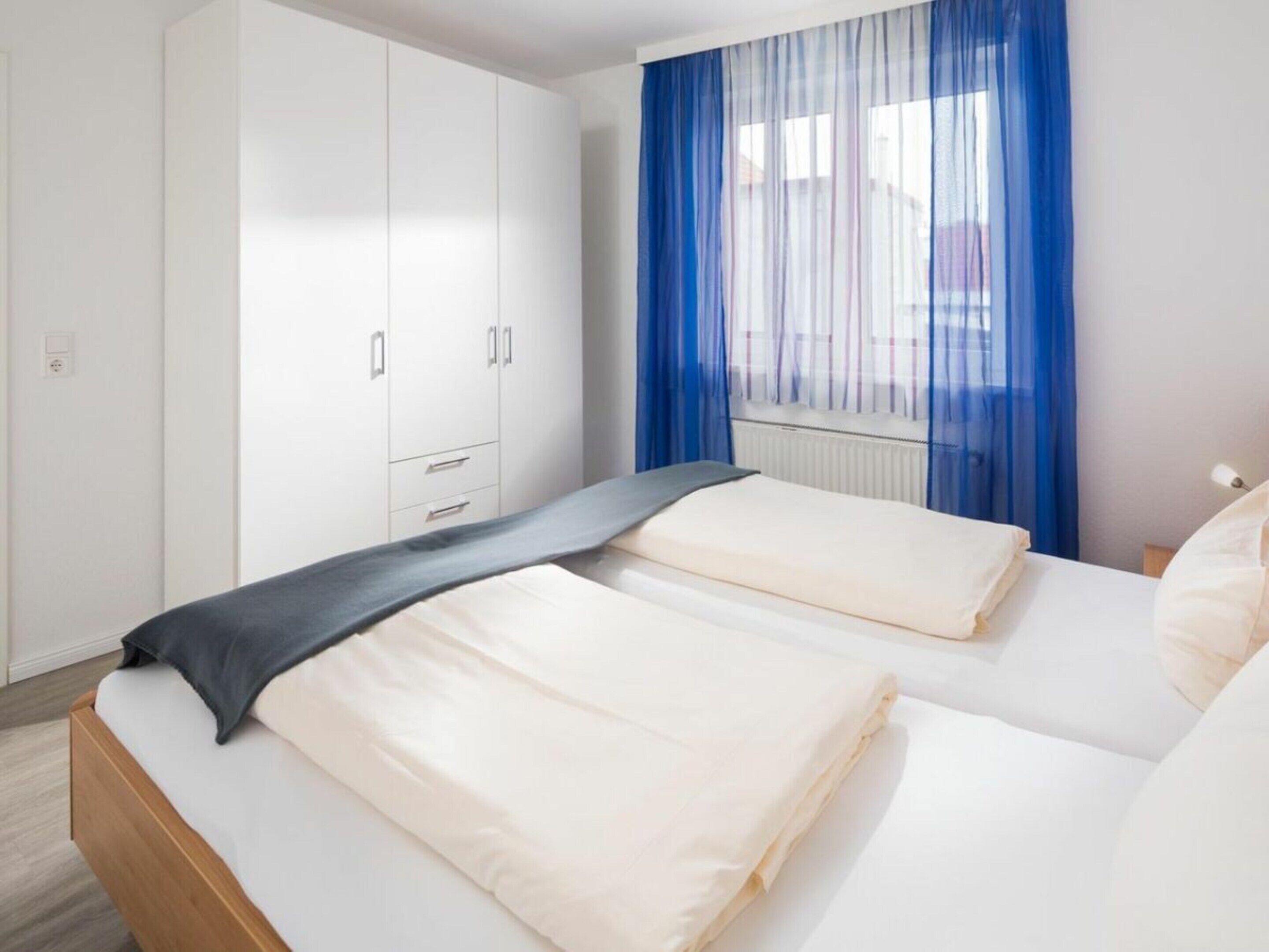 A hotel room with two beds, a wardrobe, and a window with blue curtains.