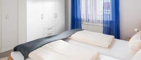 A hotel room with two beds, a wardrobe, and a window with blue curtains.