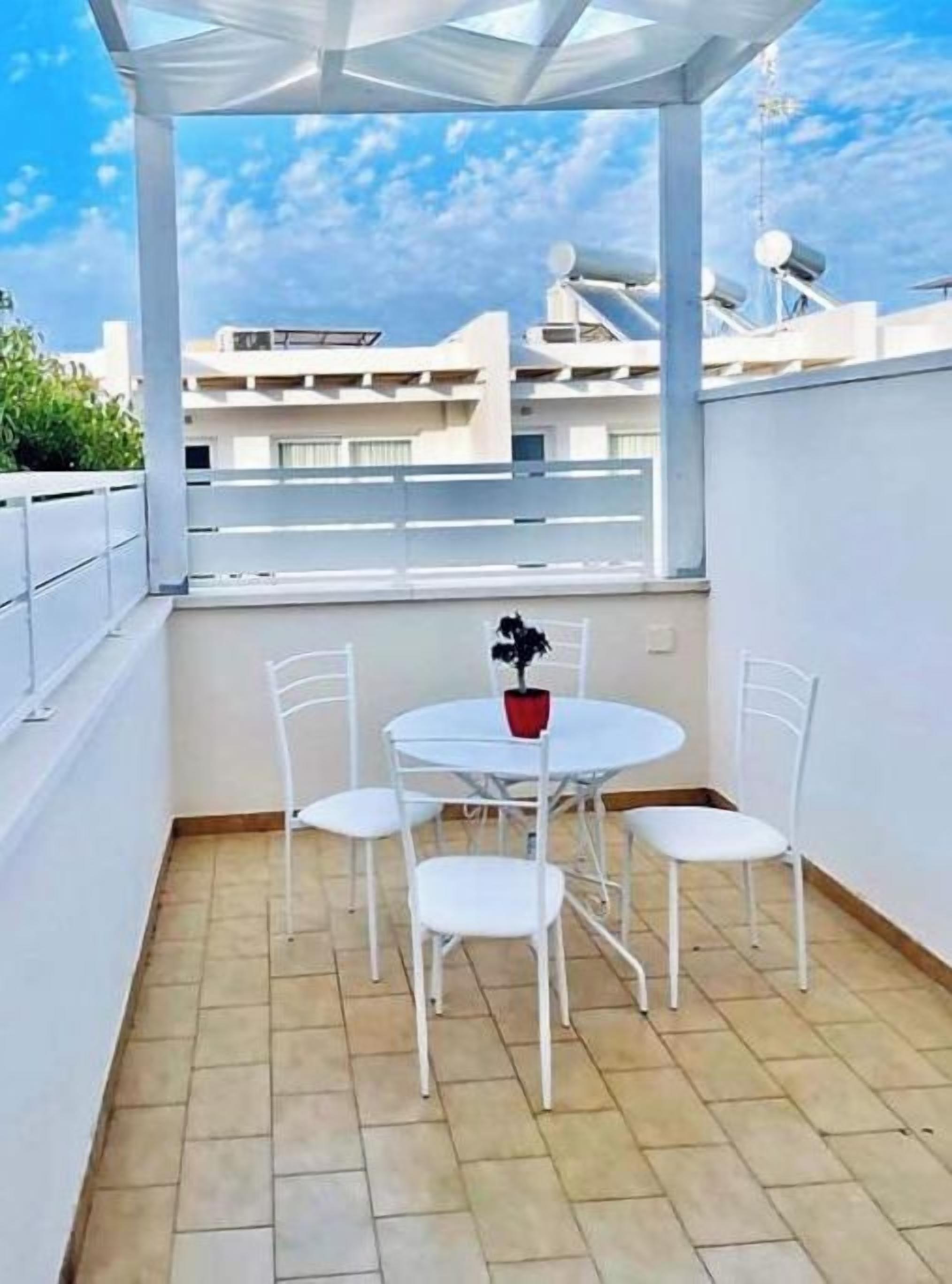 Ein kleiner Balkon mit Sitzgelegenheit, einem Tisch, einer Pflanze und Blick auf Gebäude im Hintergrund.