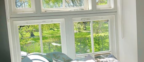 A room with a window overlooking a garden, a sofa with patterned cushions, and a decorative curtain.