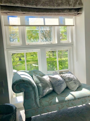 A room with a window overlooking a garden, a sofa with patterned cushions, and a decorative curtain. - Your London Home - walk to Big Ben, Westminster, river Thames (london)
