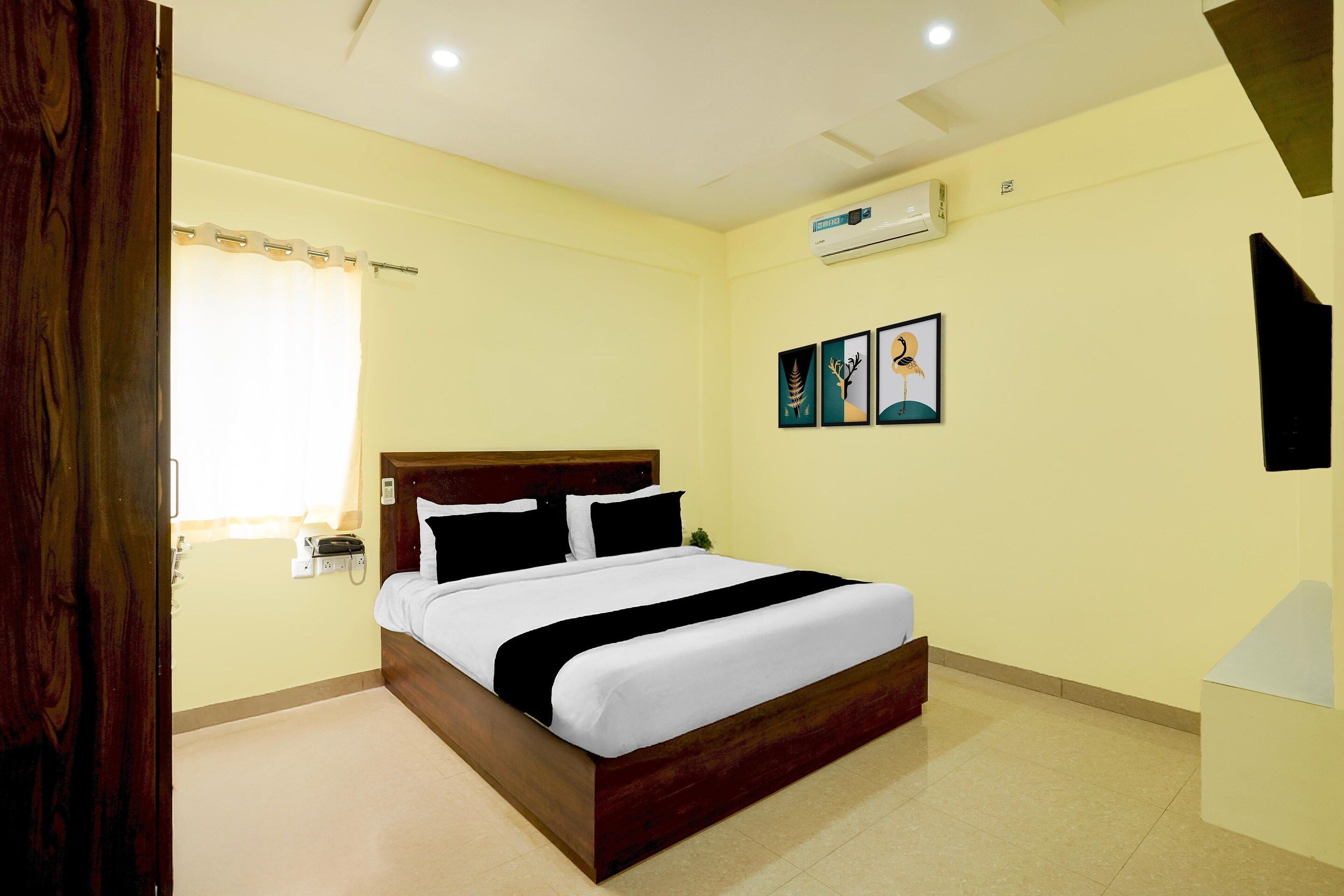 A hotel room with a bed, a telephone, an air conditioning unit, and artwork on the wall.