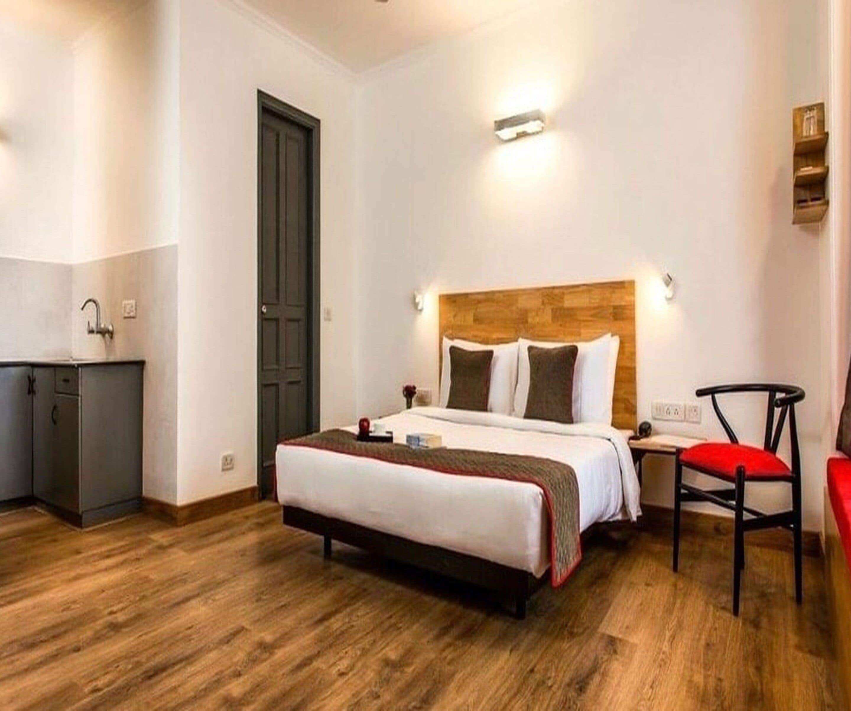 A hotel room with a bed, bedside table, chair, and a small desk with a chair.