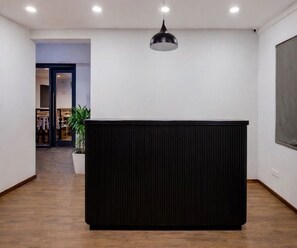 Een receptiebalie met een modern design, een potplant en een uitzicht op een kledingwinkel op de achtergrond.