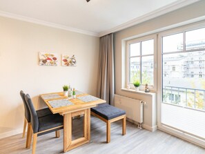 Ein modernes Wohnzimmer mit einem Holzesstisch, zwei Stühlen, einer Heizung und einem großen Fenster mit Blick auf die Stadt.