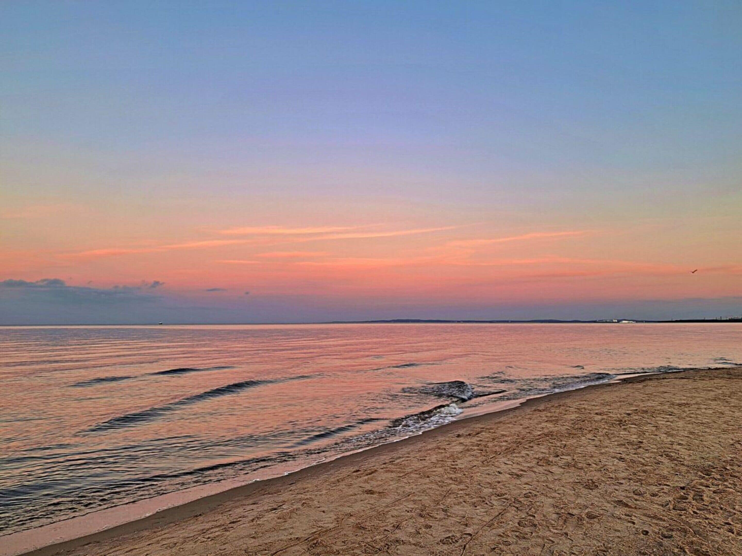 Une plage avec une mer calme et un ciel dégagé au coucher du soleil.