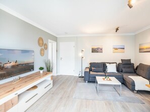 Ein modernes Wohnzimmer mit Flachbildfernseher, grauen Sofas, einem Couchtisch und einer Holz-TV-Konsole.