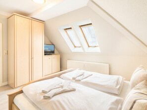 Ein Schlafzimmer mit zwei Betten, einem Kleiderschrank, einem Fernseher auf einem Schrank und Dachfenstern.