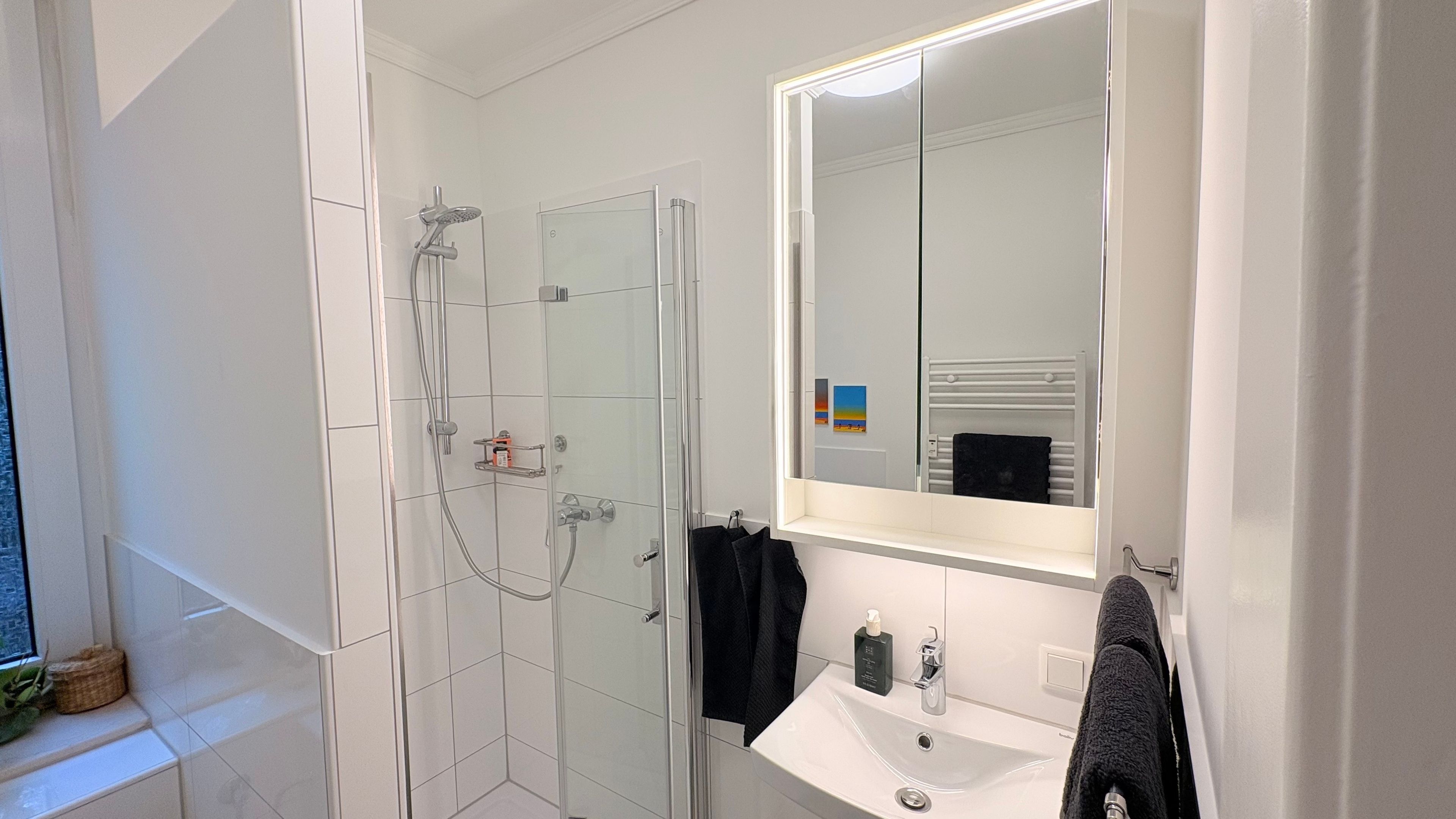 Ein modernes Badezimmer mit einer gläsernen Duschkabine, einem weißen Waschbecken und einem großen Spiegel.