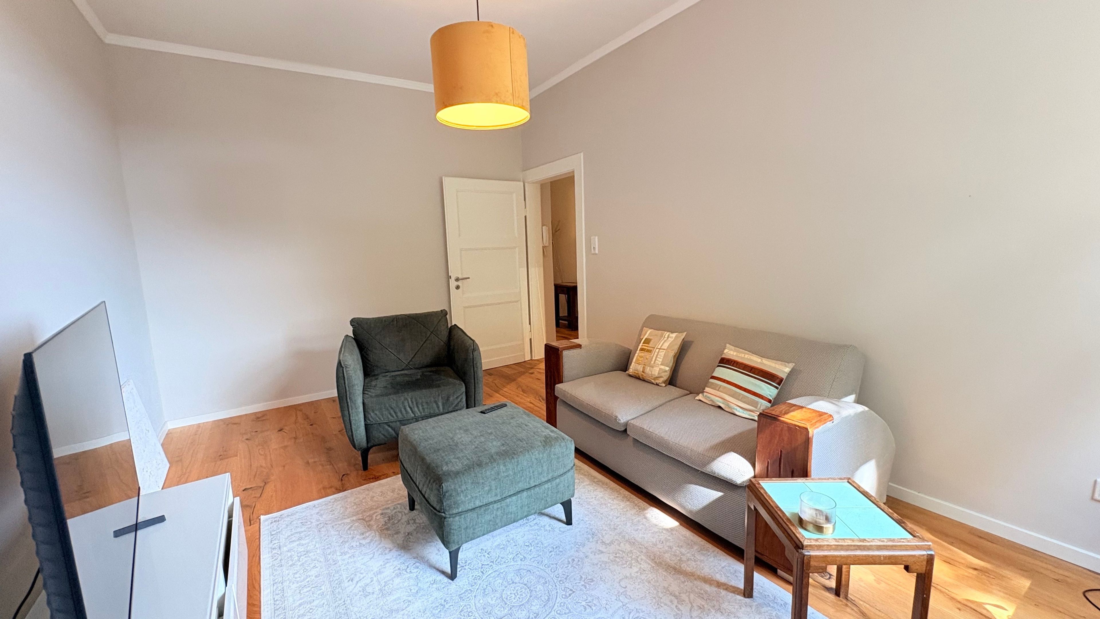 Un salon comprenant un canapé, un fauteuil, un pouf et une petite table avec un verre.