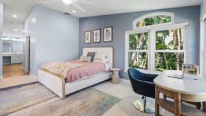 Ein Schlafzimmer mit Bett, Schreibtisch, Stuhl, einem Fenster mit Blick auf Grünflächen und einem Deckenventilator.
