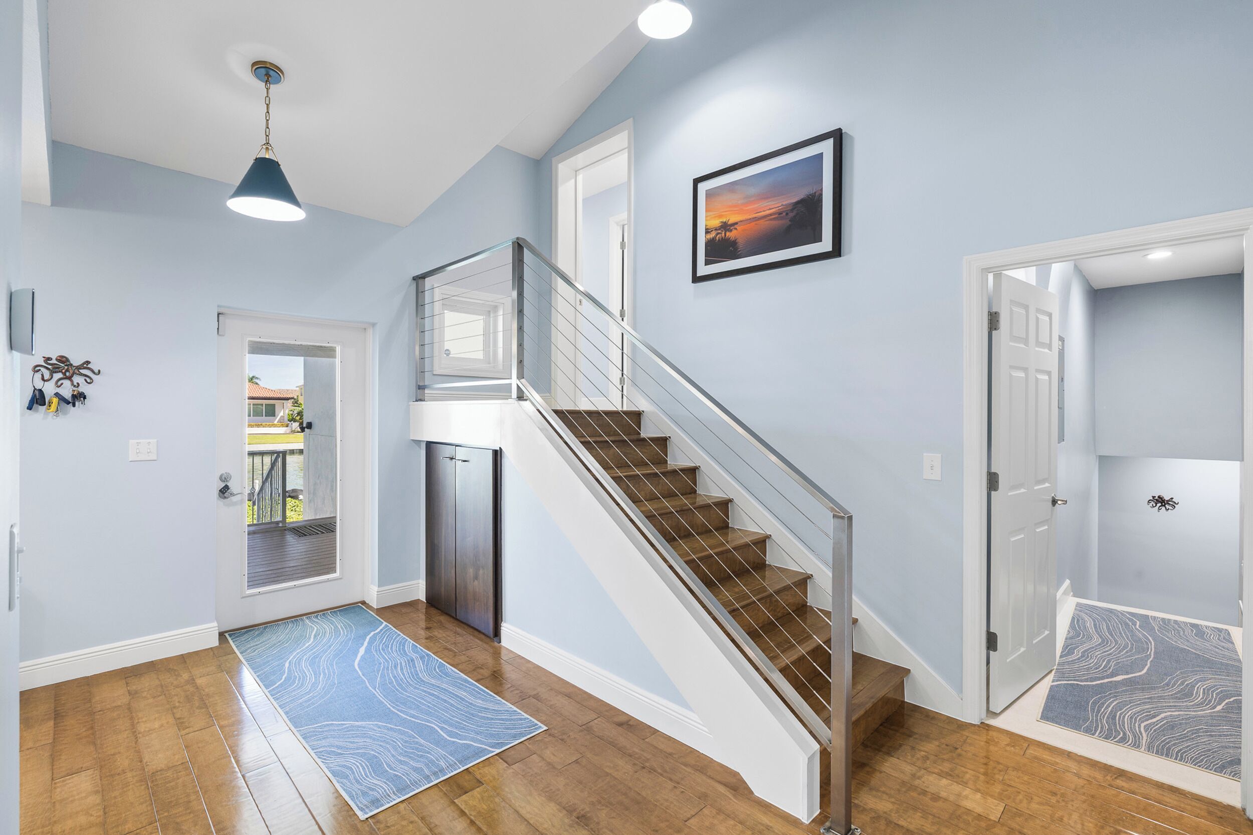 A modern interior with a wooden staircase, a view to the outside, and a blue patterned rug.
